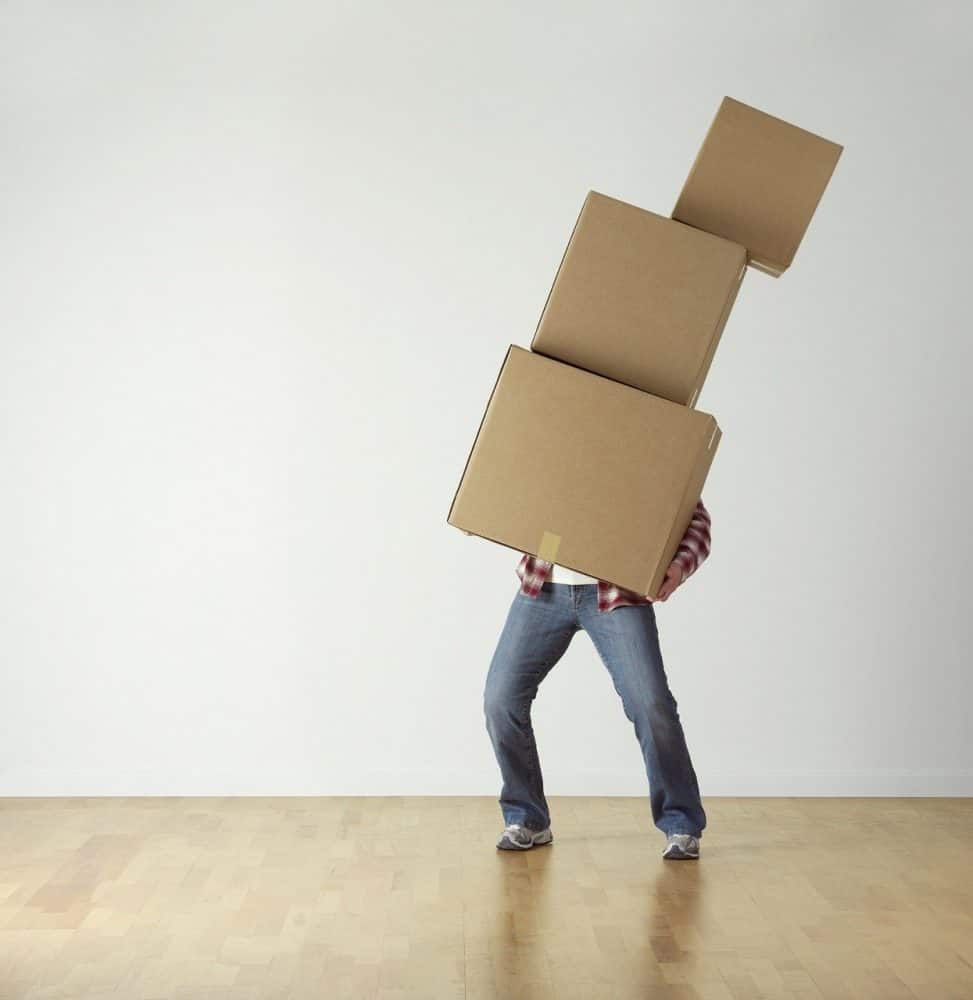 A man trying to carry three boxes stacked on top of one another. 