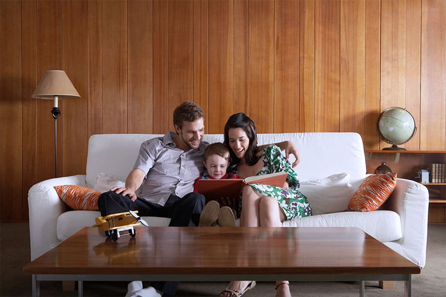 A mother and father sit with their young son between them on the couch while reading him a story book.