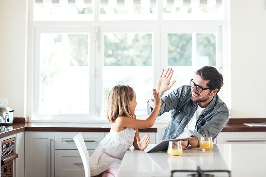A man is giving his daughter a high five as they sit at the kitchen counter.
