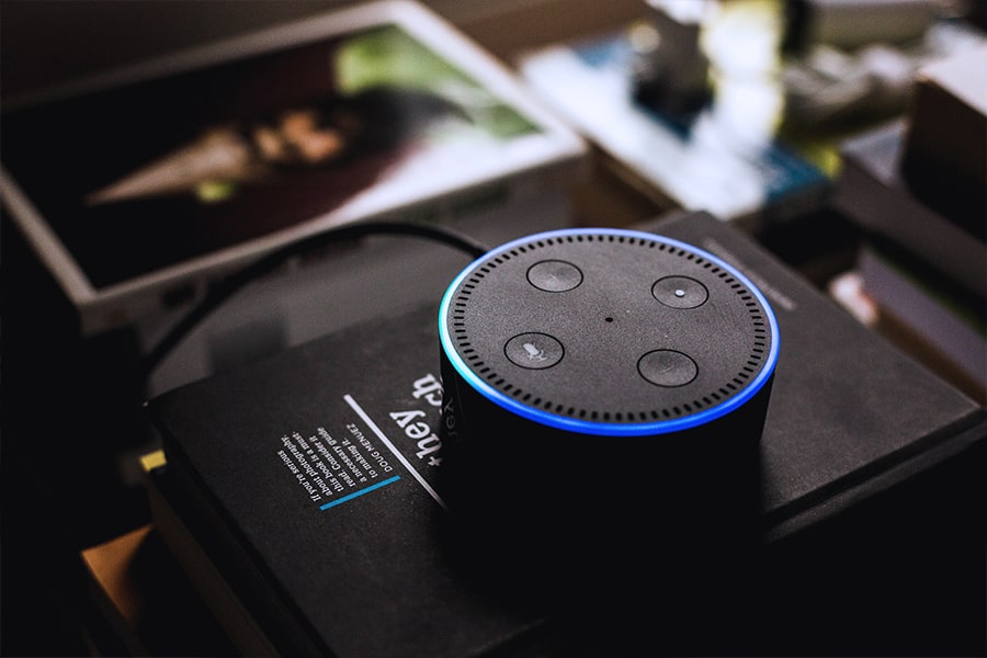 An Amazon Echo Dot with a glowing blue ring is on top of a stack of books.