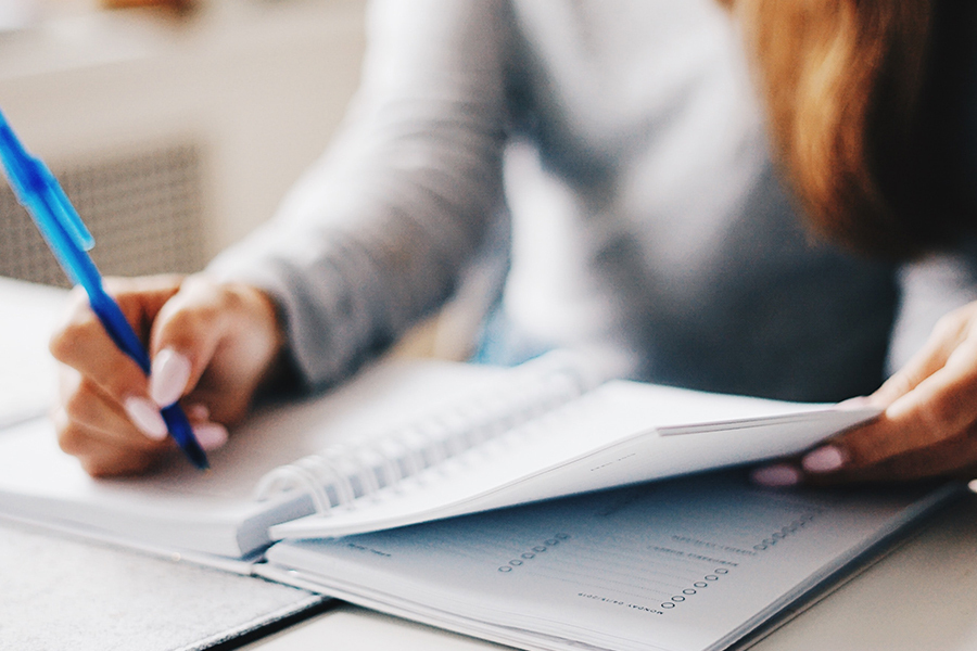 A woman is sitting at her table writing in her planner notebook.