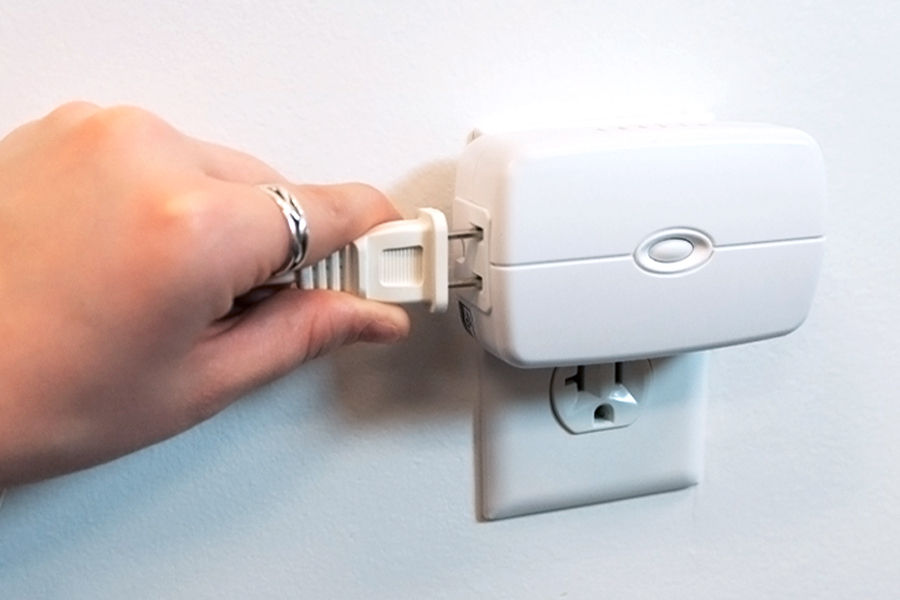A hand is plugging a power cord into a white smart plug.
